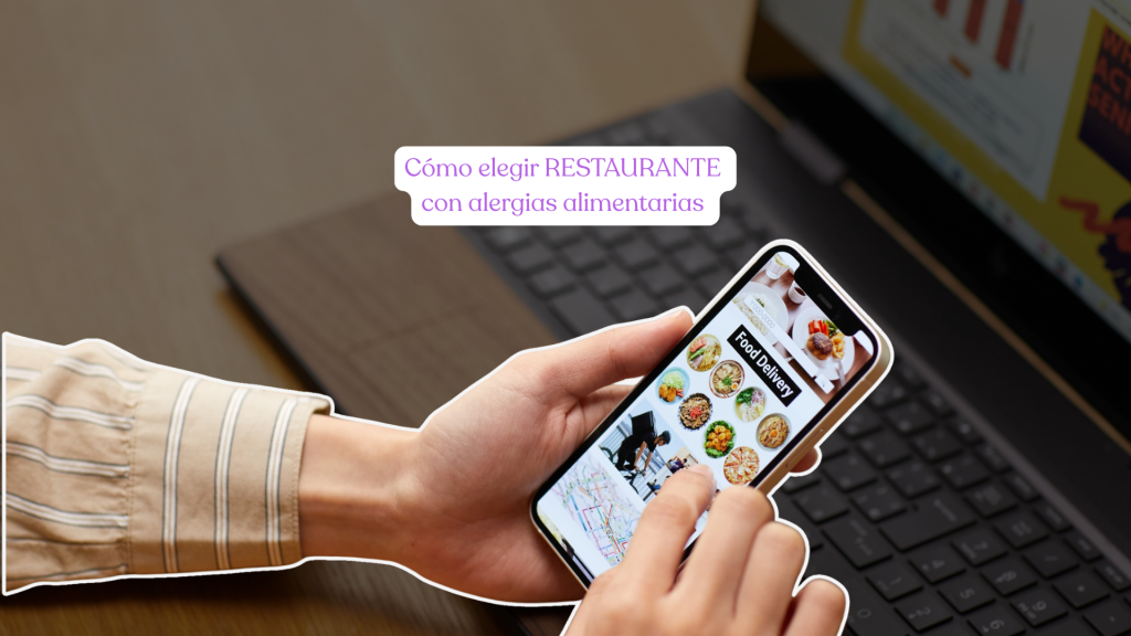 manos de una persona sosteniendo un móvil en el que hay una aplicación de restaurante a domicilio y de fondo un portátil